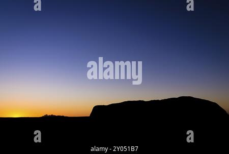 View from sunrise viewpoint of the silhouette of Uluru Ayers Rock with the sun setting behind Kata Tjuta The Olgas Stock Photo