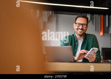 Portrait of smiling male entrepreneur messaging over smart phone while working over laptop at desk Stock Photo