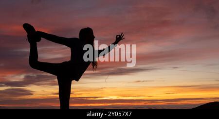 Woman doing the dancer's pose against the light at a sunrise Stock Photo