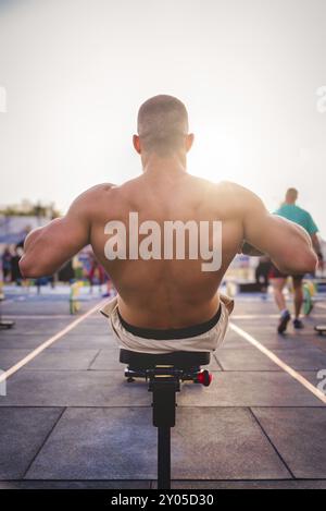 A man exercises outdoors in the sunlight, concentrating on strengthening his back muscles on a rowing machine, Barcelona, Spain, Europe Stock Photo