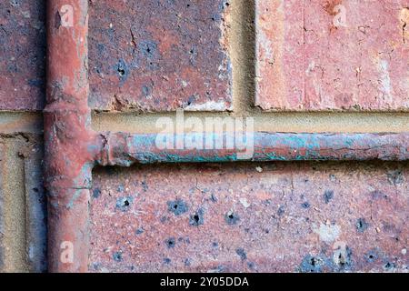 Detail of old copper water pipes subject to corrosion and limescale on the exterior of a building against a weathered cracking and flaking brick wall. Stock Photo