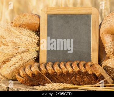 Bread and wheat on the wooden table in autumn field. Blackboard with copyspace Stock Photo