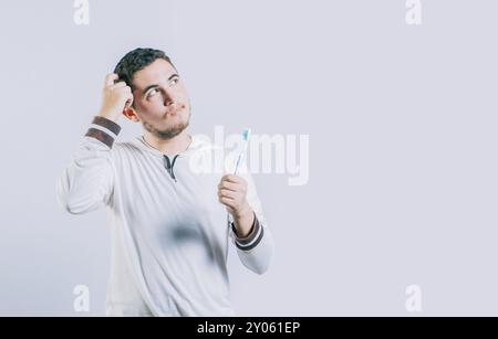 Thoughtful guy holding toothbrush looking up isolated. Worried young man holding toothbrush isolated Stock Photo