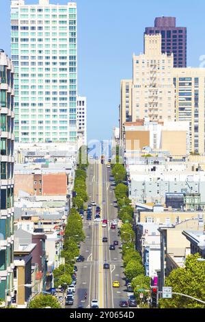 Distant telephoto view down California Street of iconic cable car and tip of Bay Bridge among residential apartment buildings on clear sunny day in Sa Stock Photo