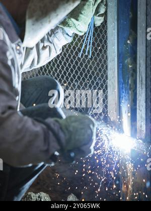 Heavy industry welder worker in protective mask hand holding arc welding torch working on metal construction Stock Photo