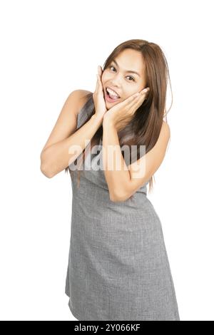 A happy, surprised Asian woman, light brown hair in gray dress cupping face, head in hands shows happy euphoria, beaming reaction to good news or info Stock Photo