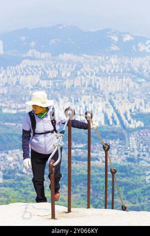 Seoul, South Korea, April 23, 2015: Korean female wearing full hiking clothes approaching Baegundae, peak of Bukhansan mountain with view of downtown Stock Photo