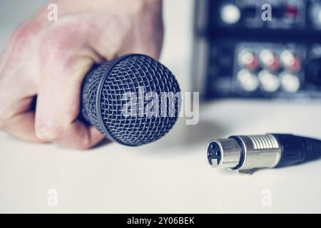 Close up picture of holding in hand microphone and audio cable, mixer in the blurry background Stock Photo