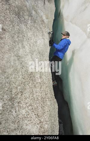 A free climber without insurance with two ice axes rises from a crack in the glacier. Free climbing without ropes Stock Photo