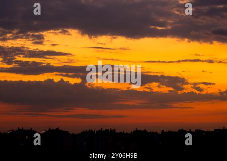 Cloudy skies over the city rooftops a few minutes after sunset. The last rays of light paint the clouds in shades of yellow and red Stock Photo