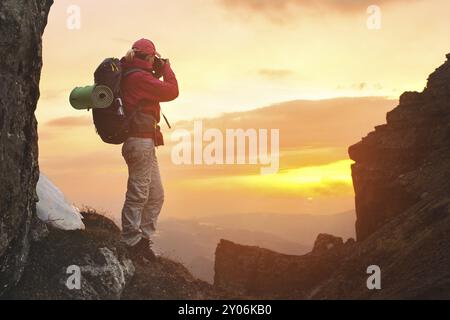 Girl photographer traveler with a backpack in the mountains photographing the sunset looking for adventure and creating masterpiece photos Stock Photo