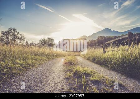 Scenic sunset view over country road, meadow, hills and mountains Stock Photo