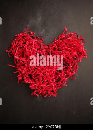 Shredded red paper shaped as a heart shape on a chalkboard, Valentines Day or Mothers Day concept background Stock Photo