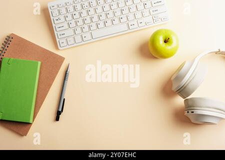 Headphones, keyboard, notepad, pen and green apple on neutral beige background. Back to school concept. Top view, flat lay, copy space. Stock Photo