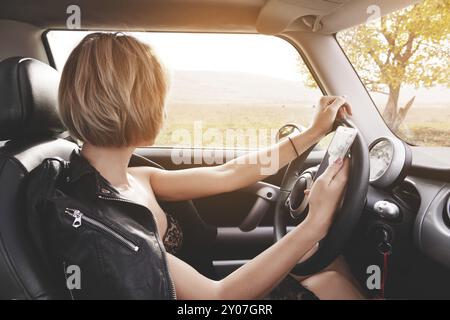 Slim girl driving a car prints text on the phone and looks out the window Stock Photo