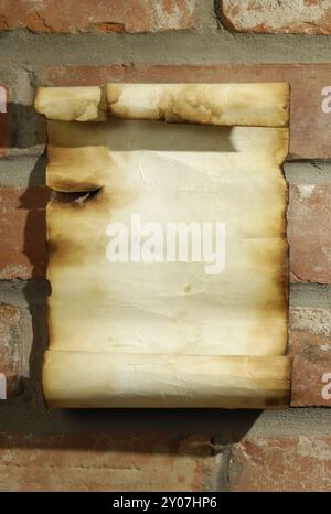 Old blank parchment with burnt edges on a red brick wall Grungy artistic background Stock Photo