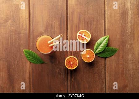 A glass of fresh orange juice with blood oranges, green leaves, and two bamboo straws, shot from the top on a dark wooden background with copy space Stock Photo