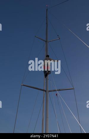 Man sitting in a bosun's chair at the main mast of a sailing yacht Stock Photo