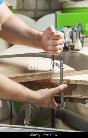 Close up Master clamps the workpiece with a dvp clamp to the workbench and on the background lies Carpentry hand router Stock Photo