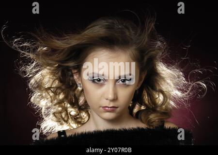 Stock photo of a Young beautiful lady face with creative make-up and flying shiny hair Artistic portrait isolated on dark red background Eleven year o Stock Photo