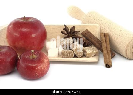 Red apples, sugar, cinnamon sticks and anise stars near rolling pin in a food still life on white, conceptual of a baking apple pie Stock Photo