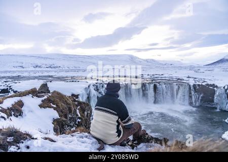 A man sitting looking at the frozen Godafoss waterfall at sunset in winter, Iceland, Europe Stock Photo