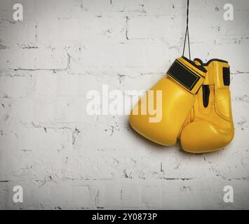 Pair of yellow boxing gloves hanging on a brick wall Stock Photo