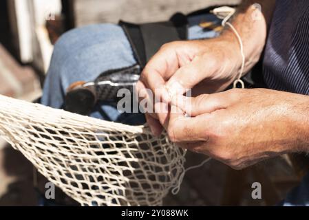 Enkhuizen, Netherlands. June 2022. The hands of a fisherman repairing fishing nets with needle and thread. Close up Stock Photo