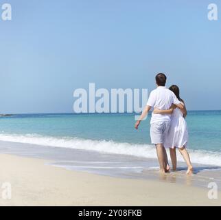 Young happy couple walking on the beach holding around each other Stock Photo