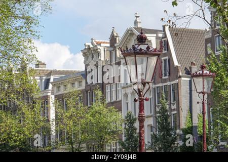 Houses and antique street lamps in front of green trees and blue sky, Amsterdam, Netherlands Stock Photo