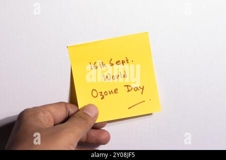 A yellow sticky note held in human hand showing world ozone day on white background Stock Photo