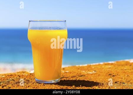 Glass filled with orange juice at blue sea with sky Stock Photo