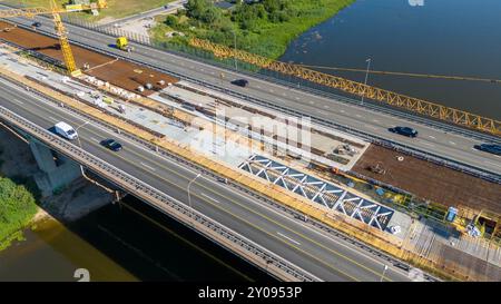 Aerial view of a construction site on a highway, featuring a large crane, construction materials, and workers. The site shows a partially completed br Stock Photo