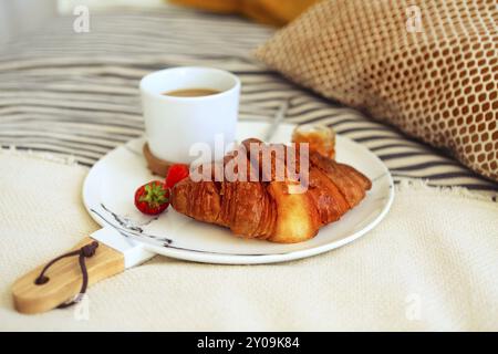 Breakfast with croissant, coffee, strawberry and jam on the plate tray in bed. Top view Stock Photo
