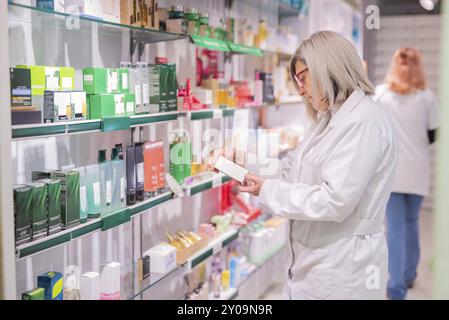 A professional pharmacist examines a product, surrounded by a variety of medicines and health supplements organized on shelves, showcasing the abundan Stock Photo