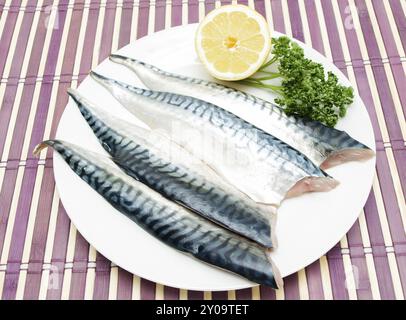 Raw mackerel fillets with half a lemon and green parsley on white plate over purple wooden table cover Stock Photo