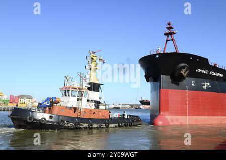 The oil tanker Unique Guaridan is towed in the harbour basin by a tugboat. Oil tanker towaged in harbour Stock Photo