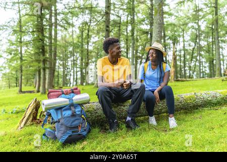 African couple sitting on a trunk in the forest during a trekking talking relaxed Stock Photo