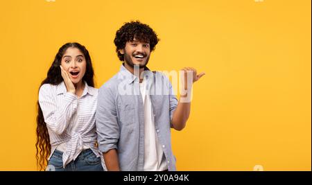 Omg, check this. Emotional indian guy pointing finger at free space, surprised lady looking at camera, panorama Stock Photo