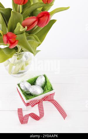 Bouquet of red tulips and gift box with chocolate aggs, easter background Stock Photo