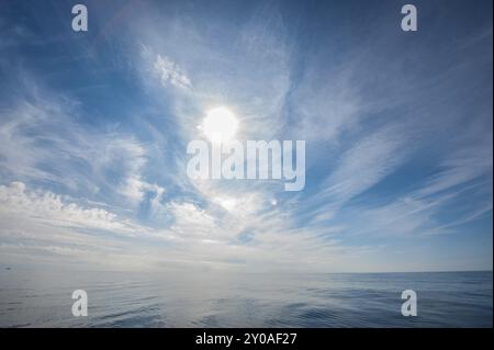 Noon sun shining through cirrus clouds over the open calm ocean Stock Photo