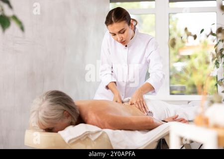 Female masseur perform lower back stroking during massage for unrecognizable mature client Stock Photo