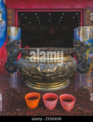 Balikpapan, Indonesia - June 22nd, 2024. A bronze incense burner with intricate dragon handles stands at the entrance of the Guang De Miao Temple in B Stock Photo
