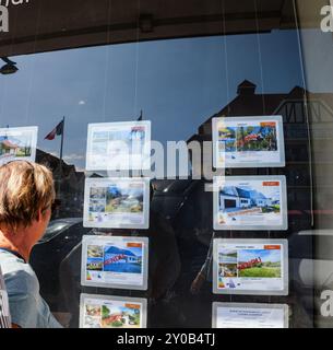 Hardelot, France - Aug 20, 2023: A person looking at real estate listings displayed in a window, showing properties for sale in a French town, with Vendu - Sold tags visible on several listings Stock Photo