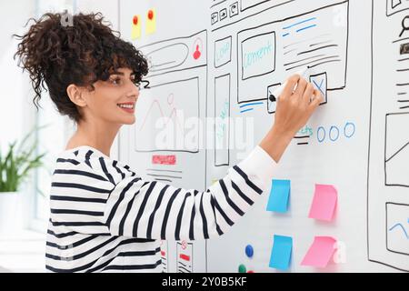 Developing UI design. Woman drawing website wireframe on whiteboard indoors Stock Photo