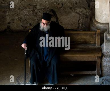 An elderly Greek Orthodox priest sitting on an old wooden bench at the entrance of the church of the holy Sepulchre in the old city of Jerusalem. Stock Photo