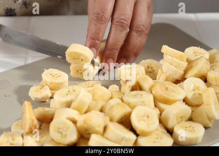 Hands of Old Female Slicing Banana on Plastic Chopping Board. Process Making Smoothies, Cake, or Cookies Stock Photo