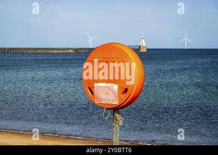 A lifebuoy at North Sea Coast, seen on South Beach in Blyth, England, UK, with Blyth Lighthouse and the pier in the background Stock Photo