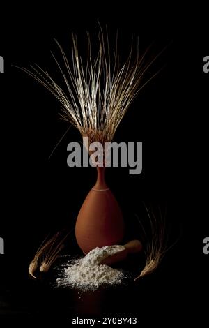 Earthenware vase with ears of wheat with wooden spoon with flour isolated on black background and copy space Stock Photo