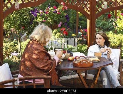 Middle age women drinking coffee in a garden outdoors. Shallow depth of field Stock Photo